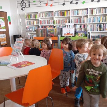 Dzieci w sali w bibliotece. 
Z tyłu regały z książkami.